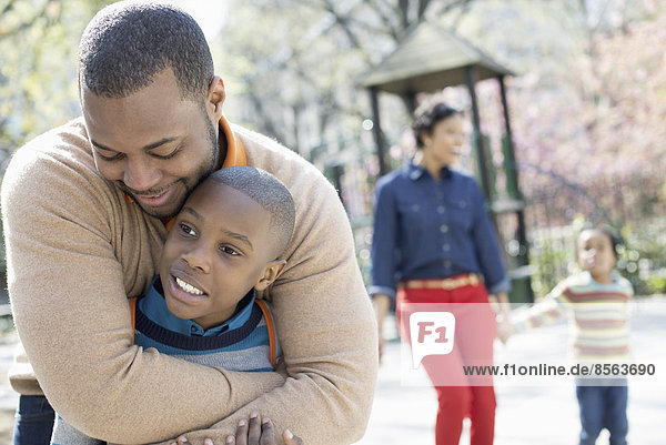 Ein New Yorker Stadtpark im Frühling. Eine Familie  Eltern und zwei Jungen  die Zeit miteinander verbringen. Ein Vater umarmt seinen Sohn.