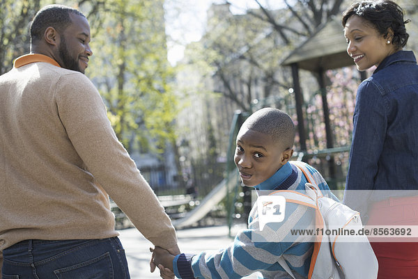 Ein New Yorker Stadtpark im Frühling. Sonnenschein und Kirschblüte. Ein Junge  der über seine Schulter schaut  zwischen seinen Eltern.