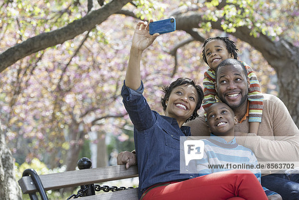 Ein New Yorker Stadtpark im Frühling. Kirschblüte. Eine Frau  die mit ihrem Smartphone ein Selbstfoto von ihrer Familie macht.