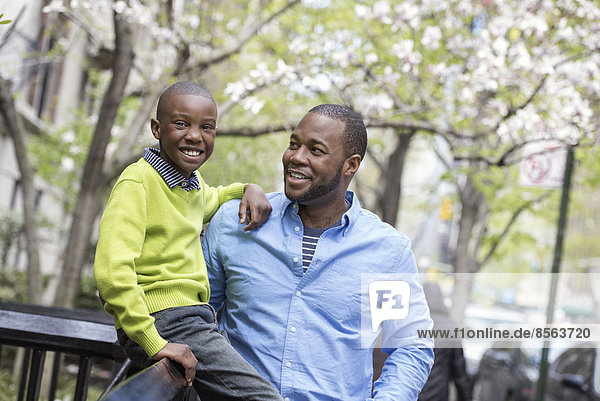 Ein New Yorker Stadtpark im Frühling. Sonnenschein und Kirschblüte. Ein Junge sitzt auf einem Zaun  neben seinem Vater.