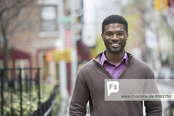 Draußen in der Stadt im Frühling. Ein urbaner Lebensstil. Ein junger Mann in violettem Hemd und Jersey lächelt.