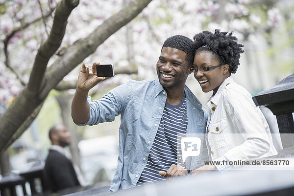 Draußen in der Stadt im Frühling. Ein urbaner Lebensstil. Ein Paar nebeneinander  Wange an Wange  das mit einem tragbaren Mobiltelefon fotografiert.