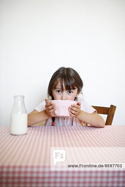 Ein kleines Mädchen sitzt an ihrem Frühstückstisch mit einer Schüssel Milch.