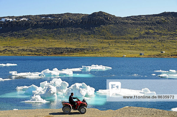 Man of the Inuit people riding a quad bike  ATM  parked on the shore of the Beaufort Sea  Arctic Ocean  Victoria Island  formerly Holman Island  village of Ulukhaktok  Northwest Territories  Canada