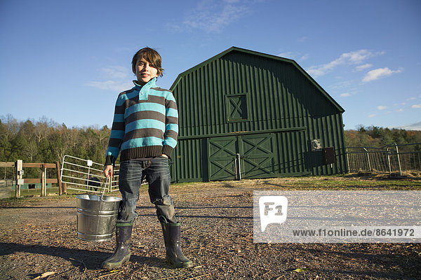 A young boy in an animal paddock  holding a bucket of feed. Animal sanctuary.