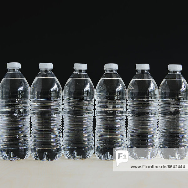 Reihe von klaren  mit gefiltertem Wasser gefüllten Plastik-Wasserflaschen in einer Reihe  auf schwarzem Hintergrund.