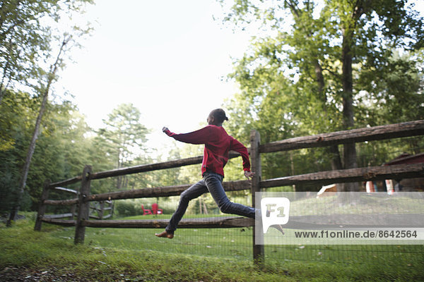 A boy running around a paddock fence outdoors.