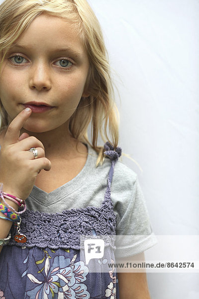 A young girl with blonde hair  and blue eyes. Her hand to her mouth.