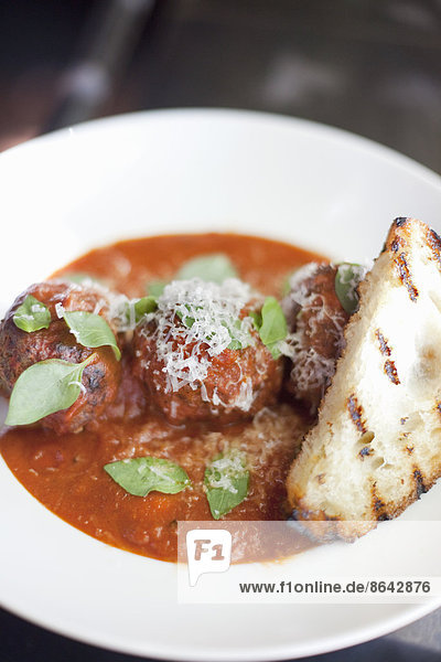 A dish of organic freshly prepared food. Grass-fed beef meatballs in tomato sauce with herb basil  shavings of Parmesan cheese and grilled bread.
