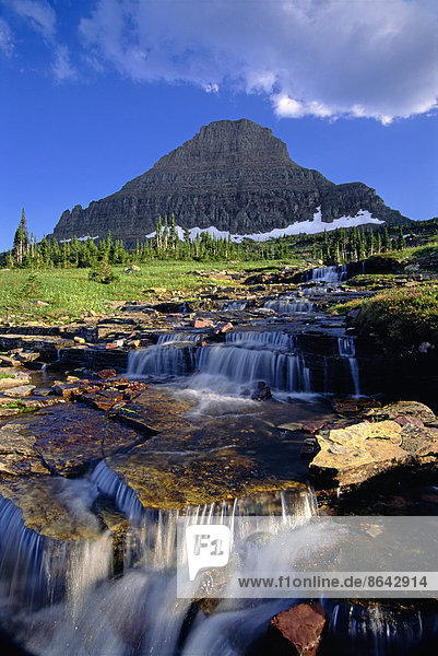 Die Landschaft des Glacier National Park  zum Gipfel des Mount Reynolds und zum Logan Pass. Wasser fließt über Felsen.