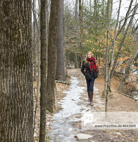 A woman in a winter coat and red scarf walking down a woodland path  in winter.