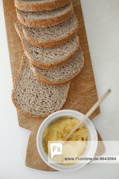 Ein hölzernes Brotbrett  auf dem ein in Scheiben geschnittenes braunes Brot ausgelegt ist. Eine Schale Butter mit einem hölzernen Buttermesser.