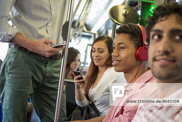 Urbaner Lebensstil. Eine Gruppe von Menschen  Männer und Frauen  in einem Stadtbus in New York City. Ein Mann mit Kopfhörern. Ein Mann und eine Frau überprüfen ihre Smartphones.