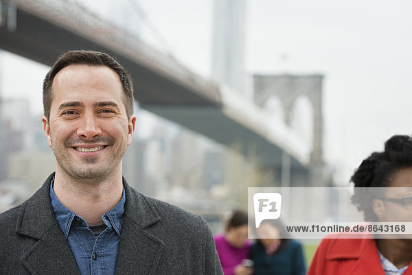 New York City  die Brooklyn Bridge  die über den East River führt. Vier Menschen  zwei Frauen  die auf ein Smartphone schauen  und ein Mann und eine Frau im Vordergrund.