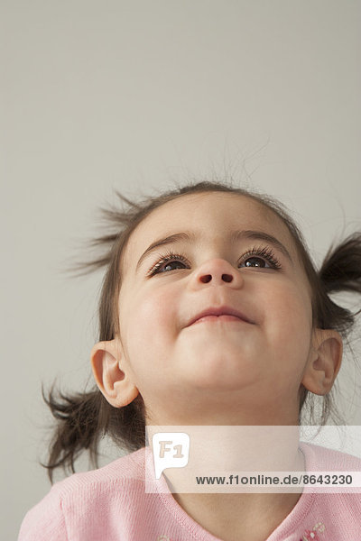 Ein junges Mädchen mit braunen Augen und dunklem Haar in Büscheln. Mit zurückgeworfenem Kopf nach oben blickend.