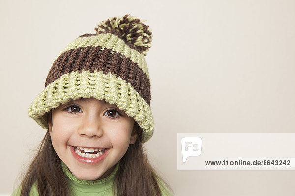 A young child with long brown hair  wearing a knitted hat with a pompom.