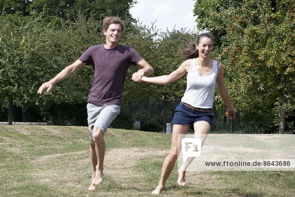 Junges Paar hält sich an den Händen und läuft im Park.
