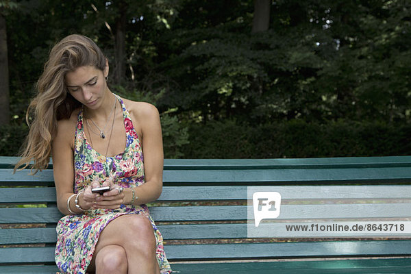Junge Frau sitzt auf der Parkbank mit dem Handy