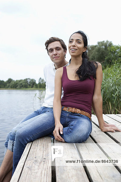 Young couple sitting on wooden pier  smiling