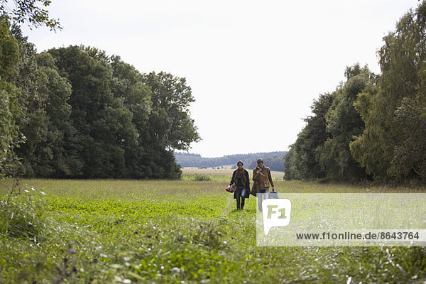 Young couple carrying camping accessories walking through field