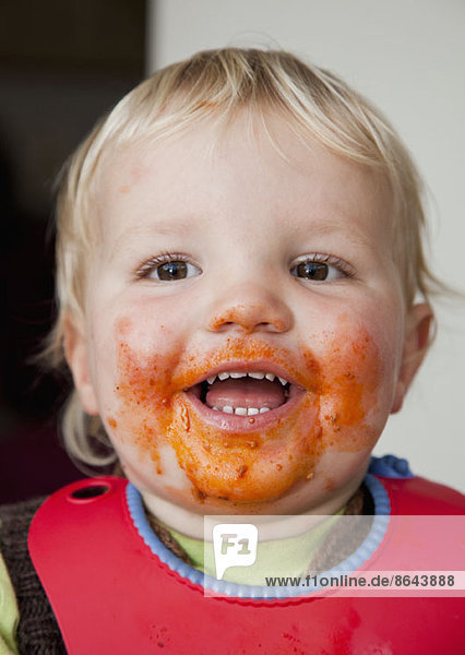 Ein lächelnder kleiner Junge mit Essen im Gesicht.