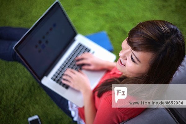 Junge Frau sitzt auf einem Teppich und tippt auf einem Laptop.