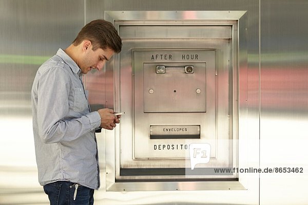 Mid adult man banking on cellphone next to bank deposit box