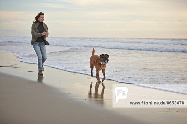 Reife Frau Spaziergang Hund am luftigen Strand