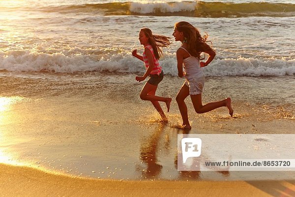 Zwei Mädchen laufen bei Sonnenuntergang am Strand entlang.