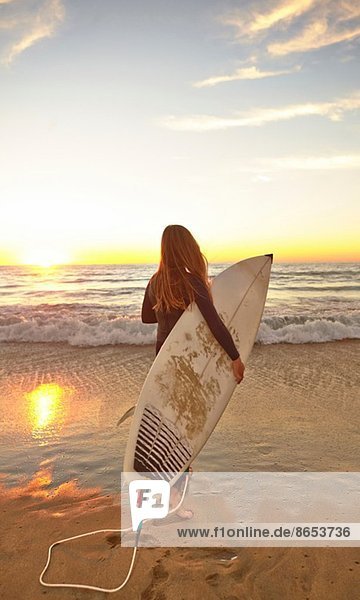 Mädchen am Strand mit Surfbrett im Neoprenanzug