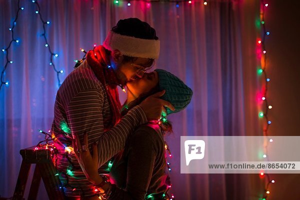 Ein junges Paar  das sich zu Weihnachten in Feenlicht gehüllt küsst.
