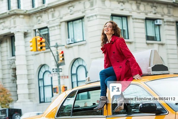 Young female tourist sitting on top of yellow cab  New York City  USA