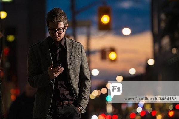 Junger Mann schlendert die Straße hinunter und schaut auf sein Handy,  Toronto,  Ontario,  Kanada.