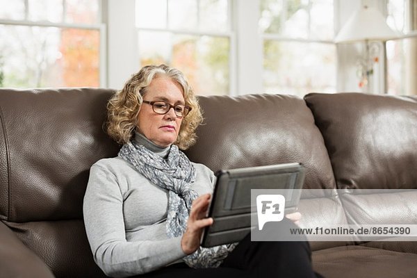Seniorin auf dem Sofa mit Blick auf das digitale Tablett