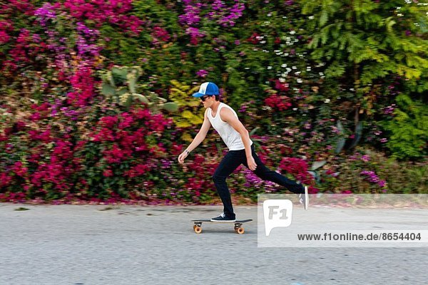 Junger Mann beim Skateboarden auf dem Bürgersteig in der Vorstadt