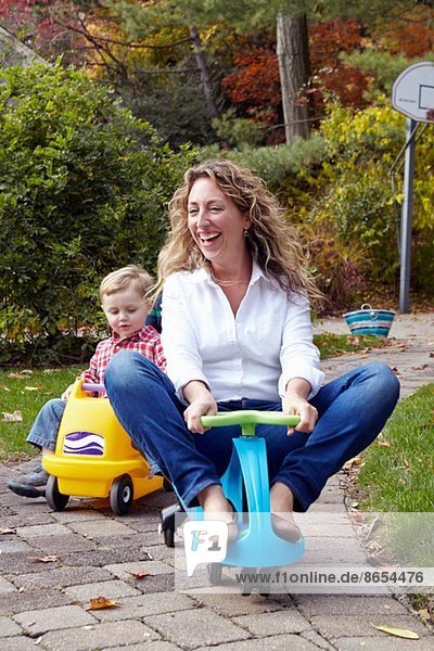 Mutter und Sohn fahren auf Spielzeugautos im Garten