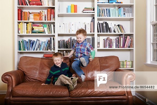 Two young brothers jumping on sofa