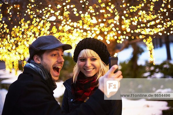 Junges Paar beim Selbstporträt mit Weihnachtsbeleuchtung im Freien