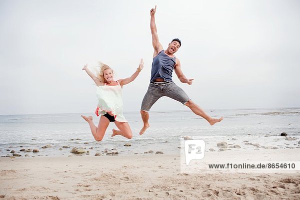 Ein schwangeres Paar springt in der Luft am Strand.