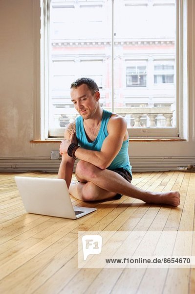 Mid Erwachsene Mann mit Laptop  während in Cowface Yoga-Pose