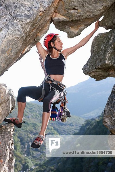 Young female rock climber balancing on rock face