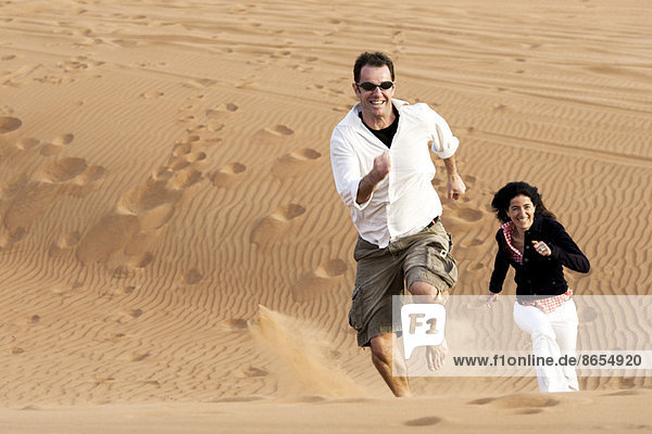 Couple running up desert dune