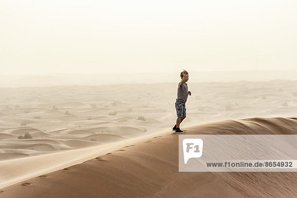 Boy walking on top of desert dune