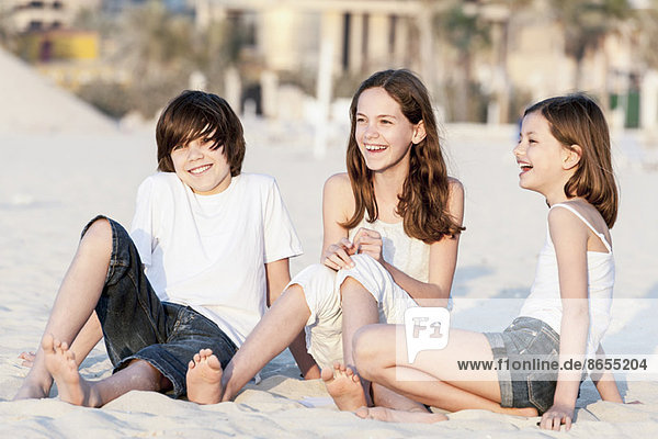 Siblings sitting together on sand at the beach