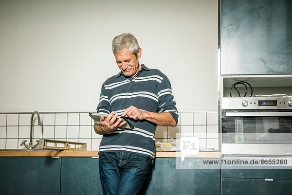 Senior Mann mit digitalem Tablett in der Küche