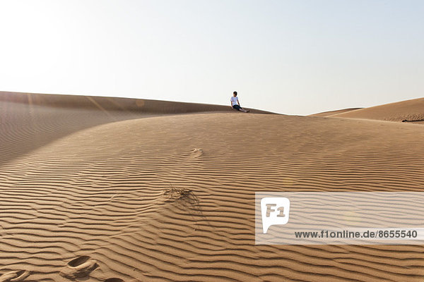 Teenage boy sitting alone on desert dune