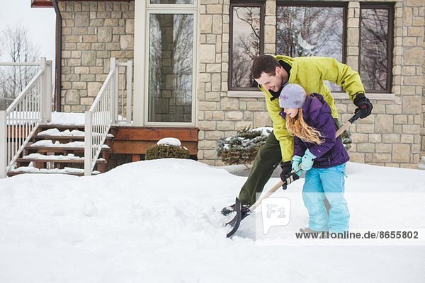Father helping daughter to shovel snow