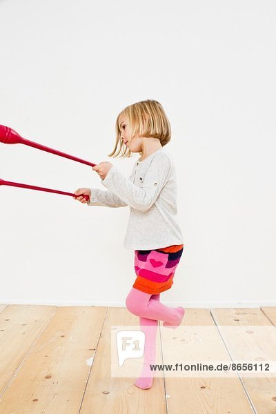 Studioaufnahme eines jungen Mädchens  das auf einem Bein jongliert.