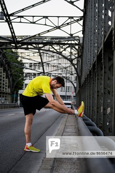 Junger Läufer  der die Beine auf der Brücke streckt.