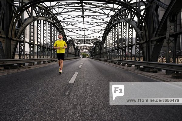 Junger männlicher Athlet  der auf der Brücke läuft
